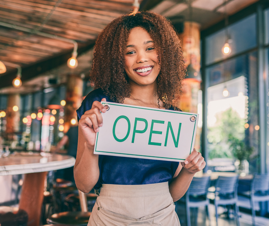 A woman holding an open sign in her new shop while thinking about Digital Marketing for new businesses.