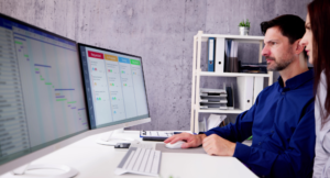 A man in a blue shirt works at a computer displaying project management and analytics dashboards. This illustrates how using AI in your social media strategy can improve content scheduling, analytics, and engagement tracking.