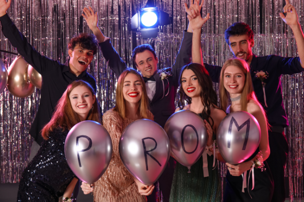Group of smiling school leavers at prom holding balloons that spell "PROM", with a sparkly backdrop and party lighting – a fun example of content ideas for school leavers.
